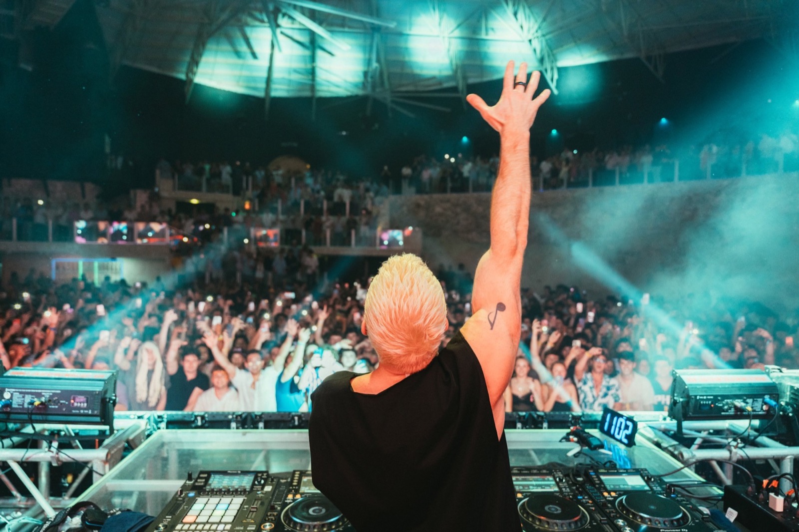 DJ with arms raised in front of a full room